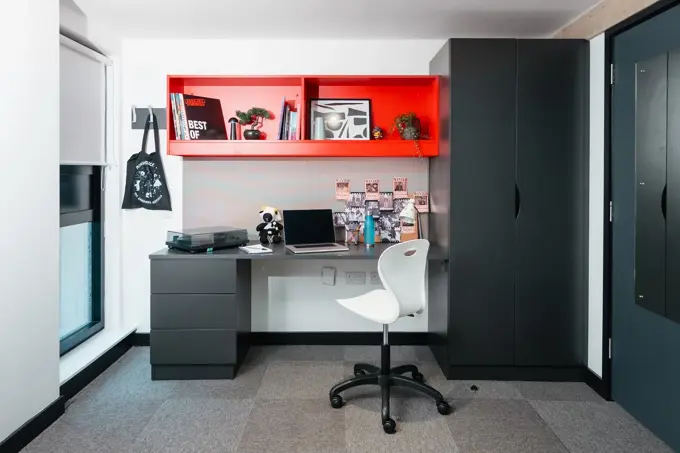Bedroom in Beton House, showing a desk and wardrobe with red shelving.